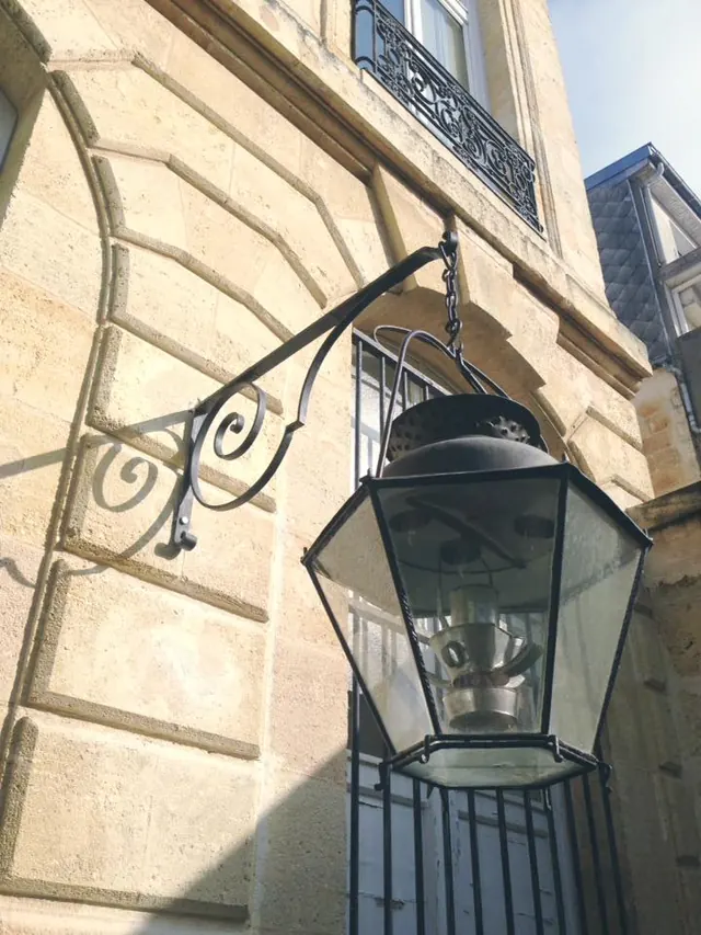 Lanterne sur potence à volutes, sur une façade en pierre